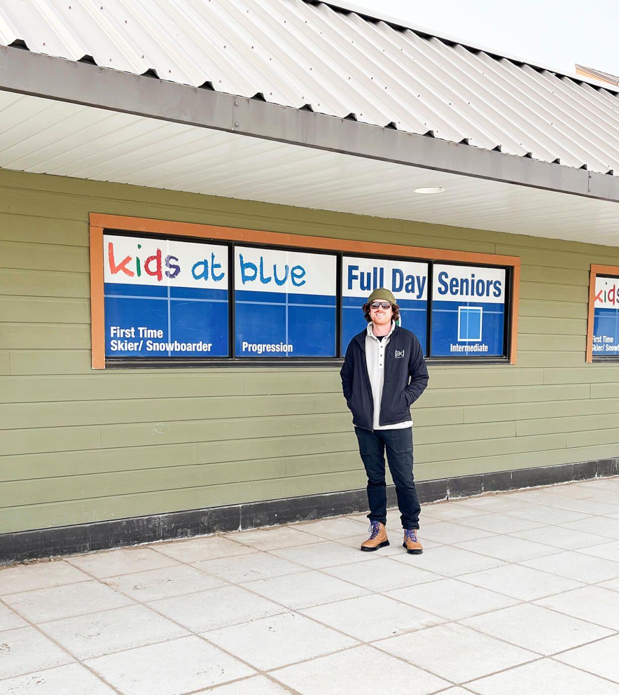 A person standing in front of a building, with copy in a window reading 'kids at Blue'